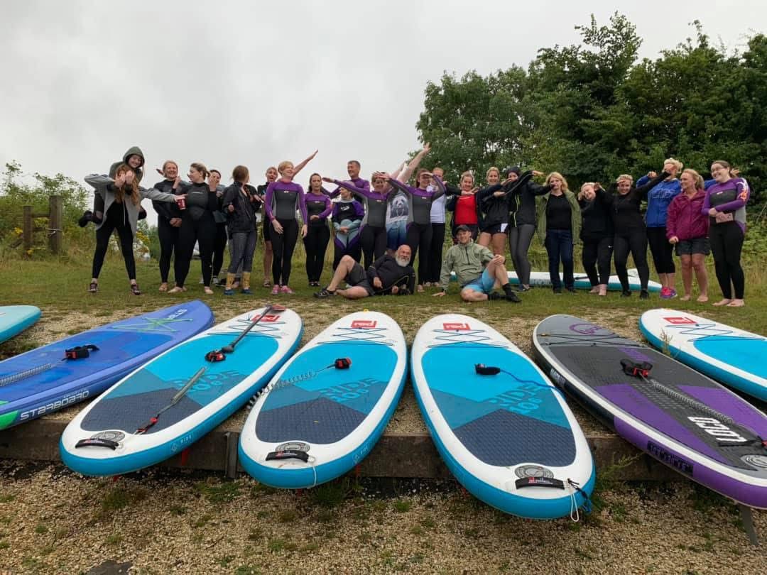 Wetsuited group cheering behind a row of paddle boards